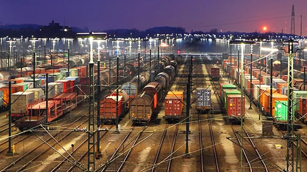 Zone de la gare avec de nombreux rails, aiguillages et lignes électriques, devant la silhouette d’une ville.