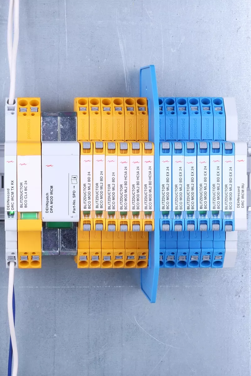 Parafoudre jaune et bleu sur une table, une armoire électrique en arrière-plan.
